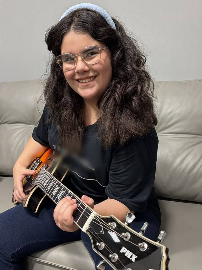 Aluna adolescente de óculos sorrindo com a guitarra no colo